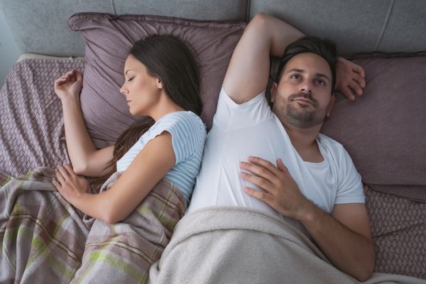 Couple in bed with lady asleep and man wide awake with insomnia