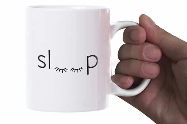 Hand holding a white mug with Sleep written on it