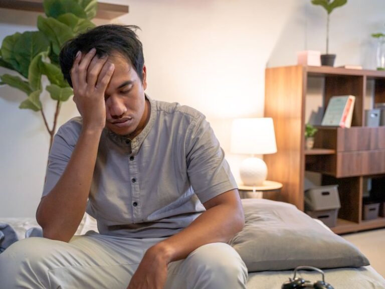 Man with his head in his hand sitting on the bed with a sleep disorder